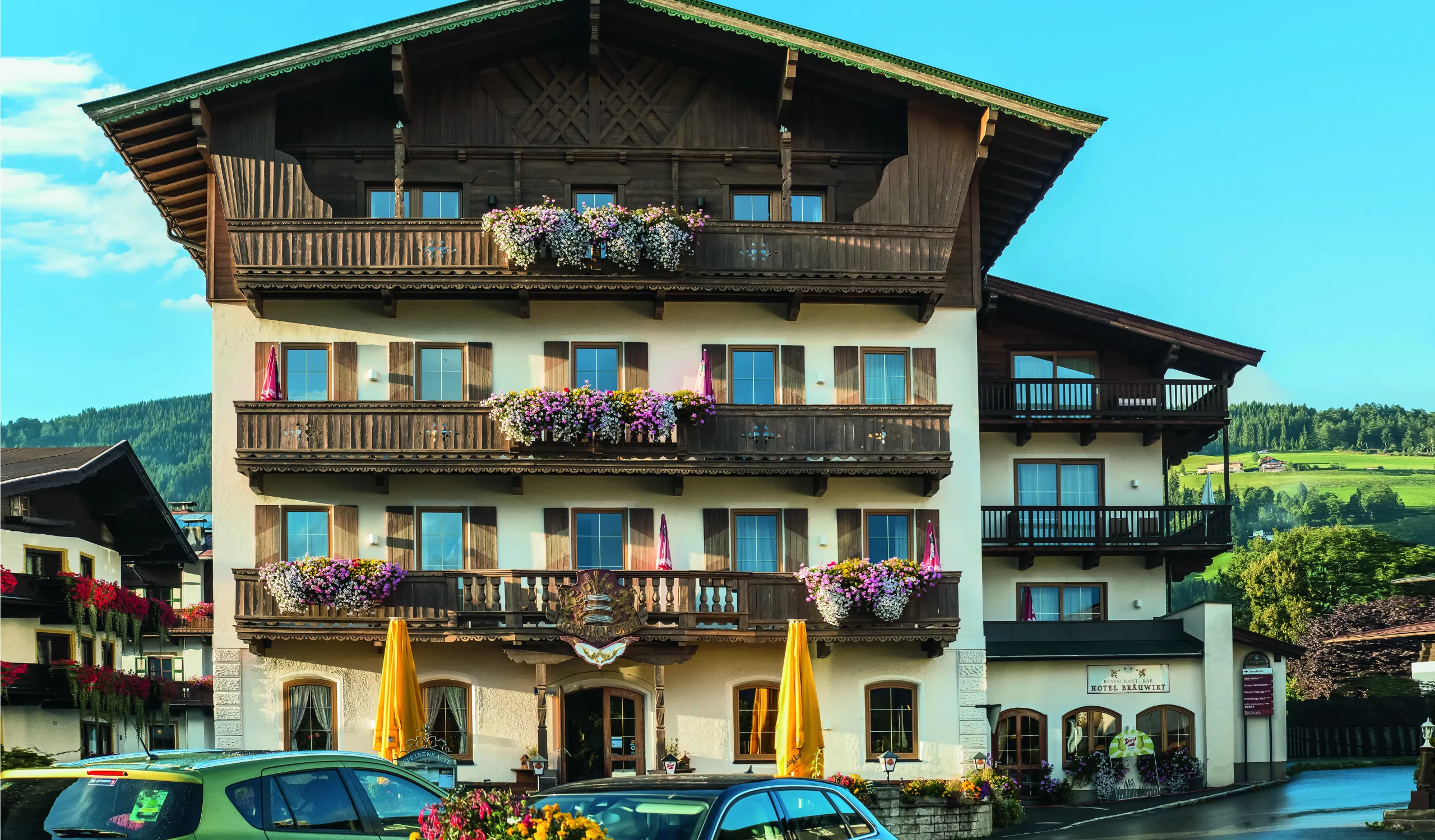 Alpenhaus mit Balkonen, blühenden Pflanzen und gelben Sonnenschirmen.