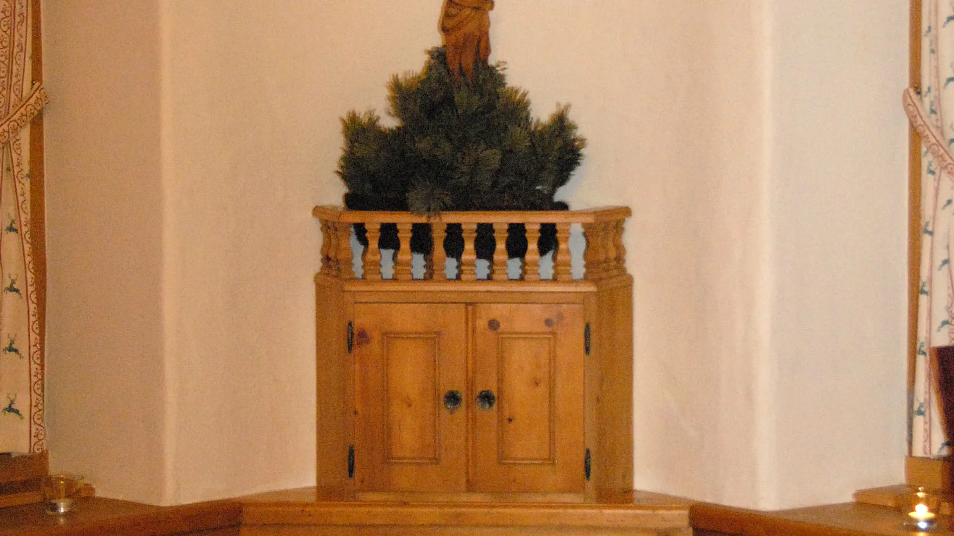 Gemütliche Ecke mit Kruzifix, Schrank und festlich eingedecktem Tisch.