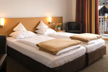 Doppelzimmer mit zwei Betten, Kissen und Decken sowie einem Sessel und Vorhängen.