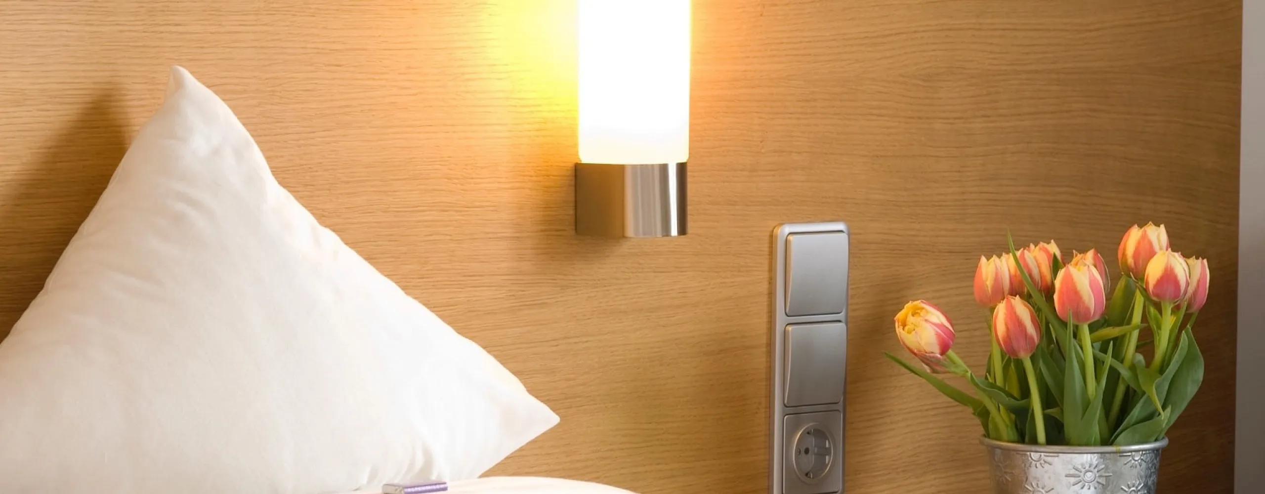 Ein Kissen und eine lampe neben einem Blumenstrauß mit Tulpen auf einem Nachttisch