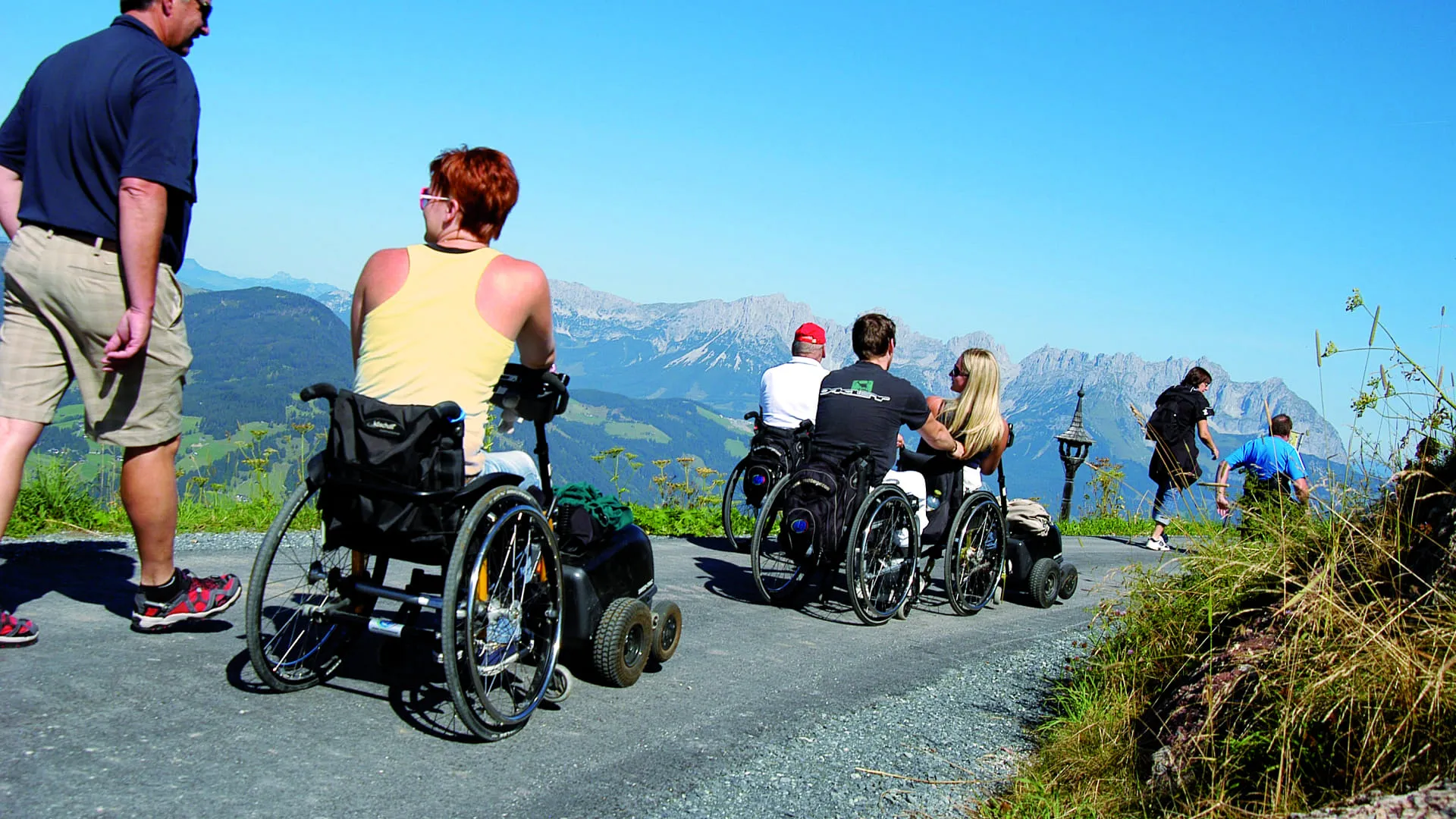 Gruppe von Menschen mit Rollstühlen auf einem Weg in den Bergen
