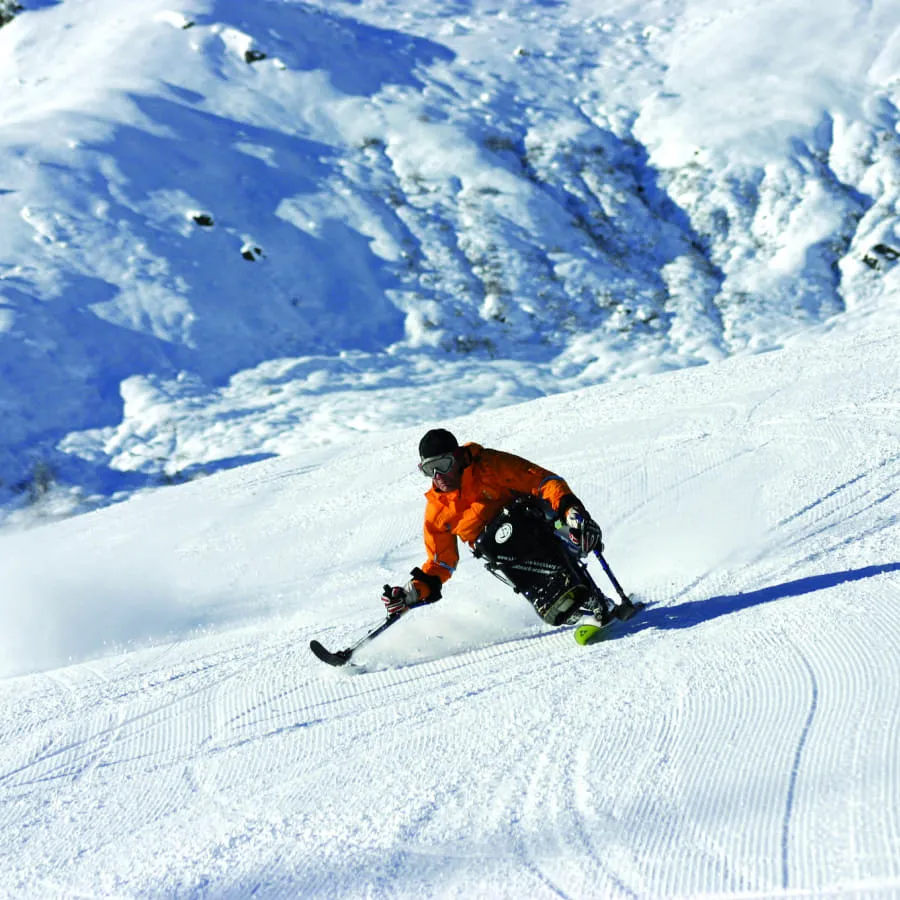 Skifahrer in oranger Jacke fährt auf schneebedeckter Piste