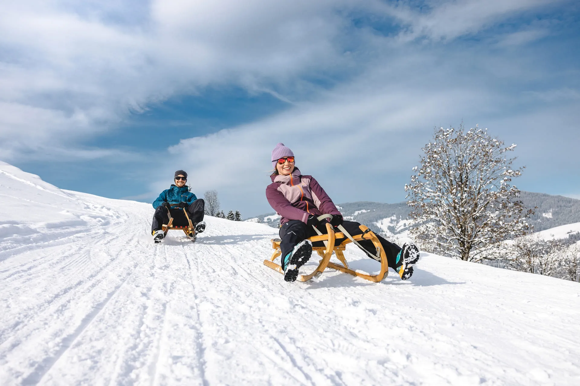 Zwei Personen rodeln auf einer verschneiten Piste im Brixental