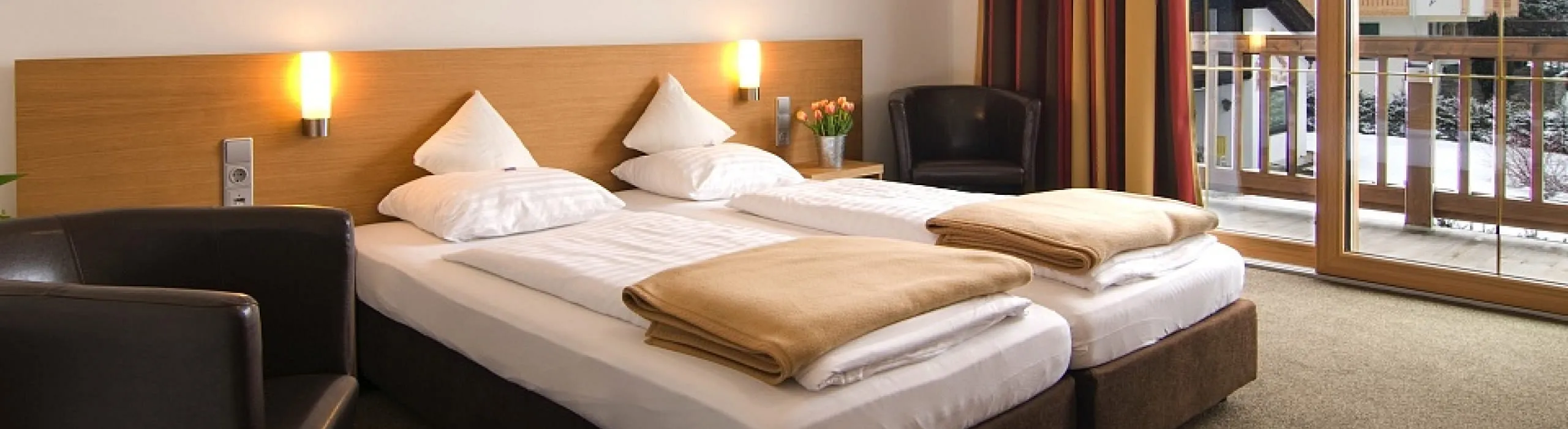 Doppelzimmer mit zwei Betten, Sesseln und Zugang zu einem Balkon